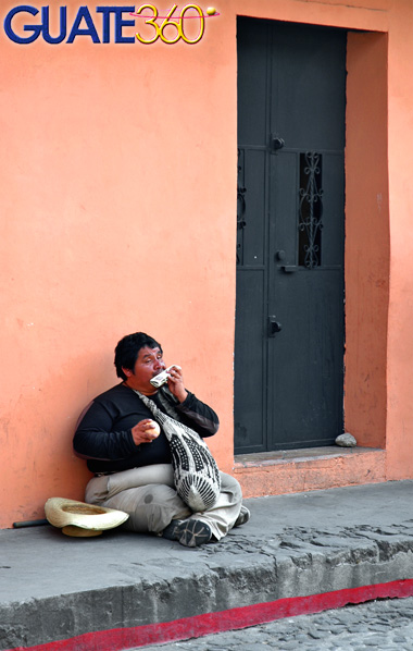 Indigente tocando harmónica frente a portal de vivienda